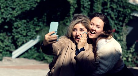 Two girlfriends take a selfie on the background of green plants.