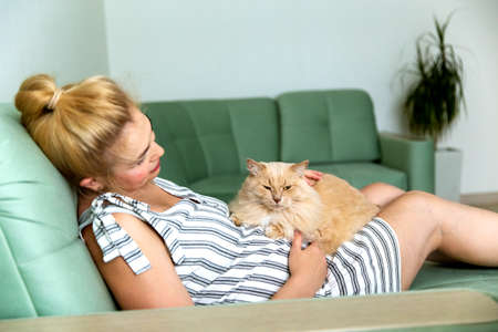 Pregnant blonde woman lying on the couch with a pet cat.の写真素材