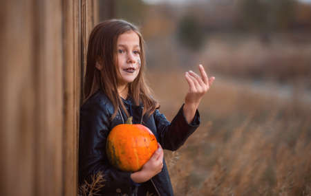Portrait of a teenage girl in dark clothes on a wooden background holding an orange pumpkin.の写真素材