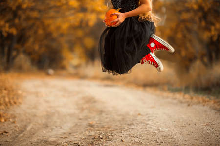A teenage girl with long curly hair is walking along a forest path. She is dressed in dark clothing. Her costume is suitable for the Halloween holiday.の写真素材