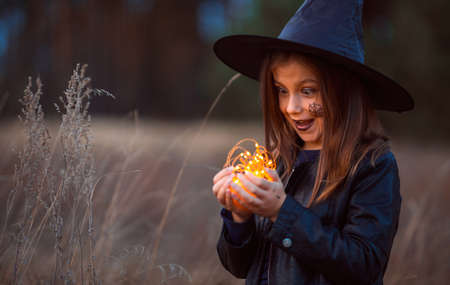 Cute teen girl in a Halloween costume outside holding lights in her hands. She has a witch's hat on her head. She's emotional.の写真素材