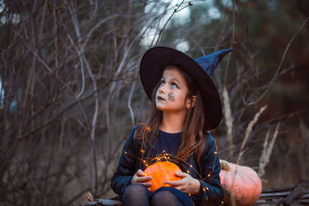 A cute girl in a Halloween costume is holding a medical face mask. Lay next to the orange pumpkins.の写真素材