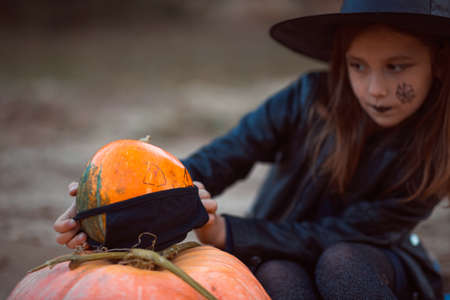 A cute girl in a Halloween costume is holding a medical face mask. Lay next to the orange pumpkins.の写真素材