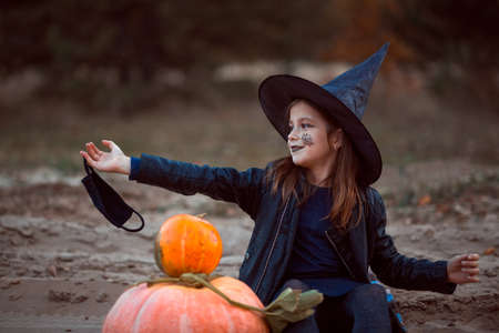 A cute girl in a Halloween costume is holding a medical face mask. Lay next to the orange pumpkins.の写真素材