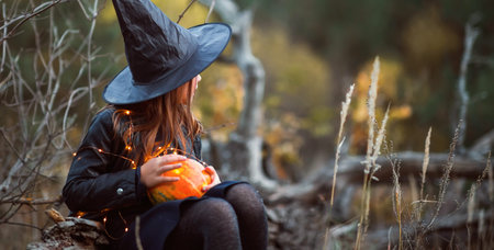 A cute girl in a Halloween costume is holding a medical face mask. Lay next to the orange pumpkins.