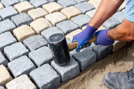 A construction worker uses a rubber mallet to set granite cobblestones in place for a new walkway or patio projectの素材