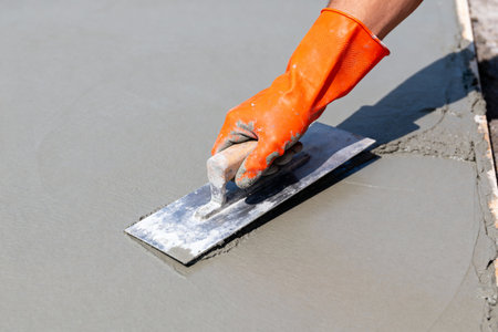 A gloved hand expertly uses a trowel to create a smooth surface on a fresh concrete pourの素材