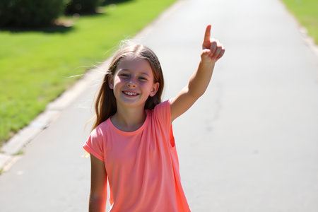 A young girl is smiling and pointing her finger up, enjoying a beautiful day outsideの素材