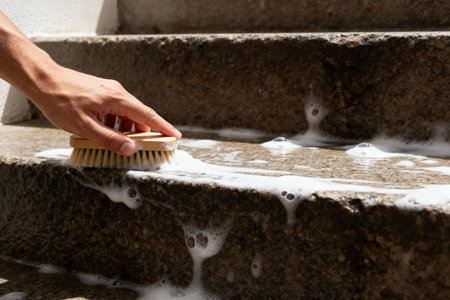 A person scrubs outdoor stone steps with a brush and soapy water, creating bubbles and foamの写真素材