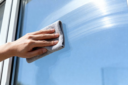 A hand wipes a window clean, leaving streaks against a bright blue sky background