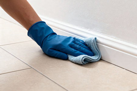 A gloved hand wipes down a white baseboard, demonstrating a cleaning task in a home or office settingの写真素材