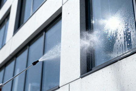 A worker uses a pressure washer to clean the exterior windows of a contemporary office building, creating a sparkling effectの写真素材