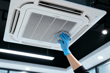 A person wearing blue gloves wipes down an air conditioner, ensuring clean air circulationの写真素材