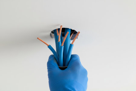 An electrician wearing a blue glove holds a bundle of electrical wires, ready for installationの写真素材
