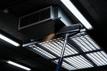 A worker is shown cleaning a ventilation system, removing dust and debris from the metal grateの写真素材