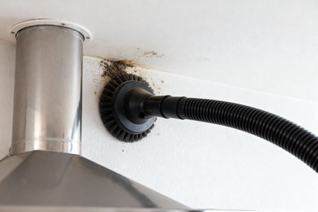 A close-up view shows the process of cleaning a kitchen range hood with a brush attachment and vacuumの写真素材