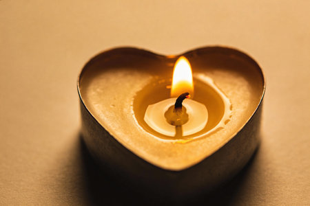 A single heart-shaped candle glows with a soft, warm flame, casting a gentle light and creating a cozy atmosphereの写真素材