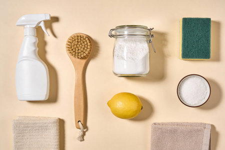 A flat lay arrangement of eco-friendly cleaning items like a spray bottle, wooden brush, baking...