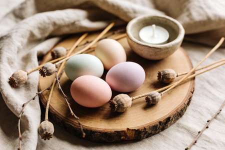 A rustic Easter arrangement featuring four pastel-colored eggs, dried poppy seed pods, and a small...