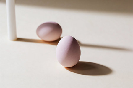 Two delicate pastel-colored eggs are arranged on a plain surface, with a tall white object casting a...