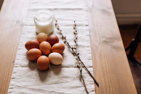 A rustic arrangement of brown and cream eggs with pussy willow sprigs and a white candle on a linen...