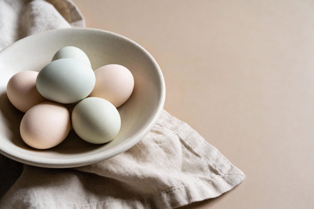 A collection of pale pink and blue-green eggs nestled in a ceramic bowl, presented on a textured...