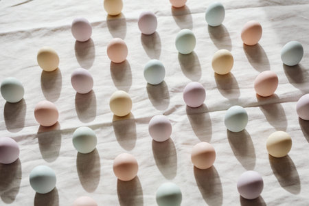 A collection of pastel-colored Easter eggs are artfully arranged in a grid pattern on a neutral...