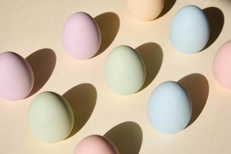 A collection of pastel-colored Easter eggs casting long shadows on a light yellow background,...
