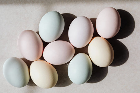 A collection of delicate pastel Easter eggs are artfully arranged on a textured surface, casting...