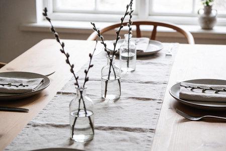 A light and airy dining table is set with plates, napkins, and clear glass vases holding delicate...
