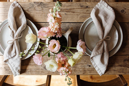 A beautifully arranged dining table with plates, linen napkins tied with twine, and a vase of delicate pink and white flowersの写真素材