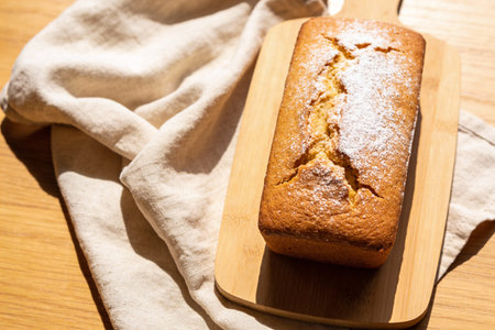 A freshly baked loaf cake with a golden crust, lightly dusted with powdered sugar, presented on a...