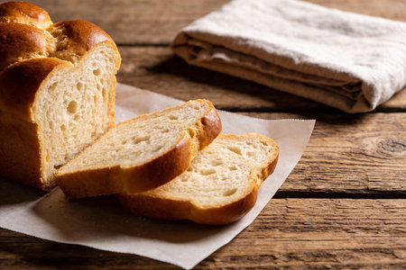 A golden-brown loaf of challah bread, sliced and ready to be enjoyed, remains on parchment paper...