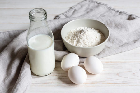 A simple still life composition featuring essential baking ingredients including a glass bottle of...