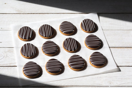 A dozen oval-shaped cookies are neatly arranged on white parchment paper, each topped with dark...