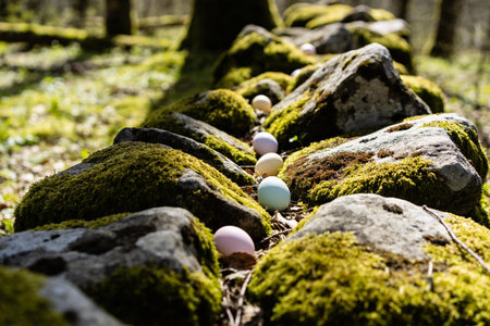 Pastel colored Easter eggs are artfully placed along a natural stone wall covered in vibrant green...