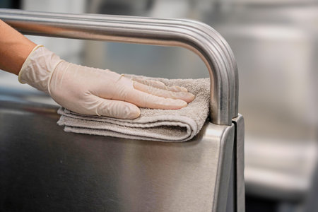 A close-up shot shows a hand wearing a white latex glove meticulously cleaning a metallic railing...