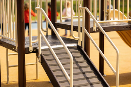 Focus on the steps and railings of a contemporary playground, with blurred figures of children enjoying outdoor activities in the distanceの写真素材