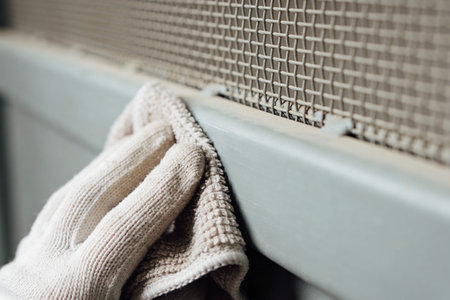 A hand wearing a textured glove gently wipes away accumulated dust from a surface next to a metal grate, highlighting a cleaning processの写真素材