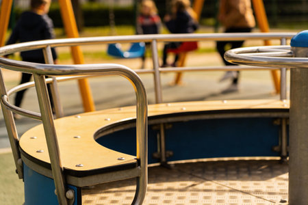 A close-up view of a merry-go-round with children blurred in the background enjoying the playground on a bright dayの写真素材