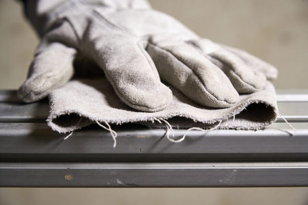 A detailed view of a well-used leather glove and a piece of fabric on a textured metal bar, suggesting manual labor or constructionの写真素材