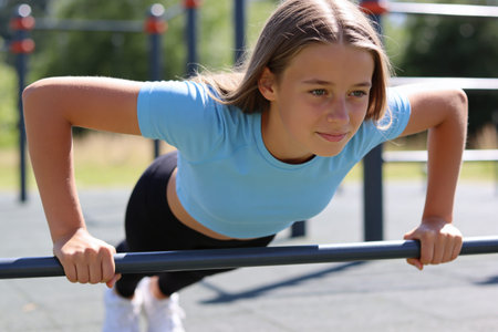 A determined young girl focuses intensely while performing a challenging push-up exercise on a metal...