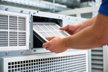 A person's hands are shown carefully removing a used air filter from a complex mechanical unit,...