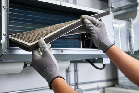 A close-up shot shows a person in protective gloves carefully extracting a clogged air filter from...