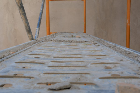 A low-angle view of a weathered scaffolding platform covered in dust and debris, with orange support...
