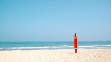 Surfboard resting on a white sand beach with ocean waves rolling in the distance. Suitable for surf school promotions, tropical travel guides, or summer lifestyle blogs.の写真素材