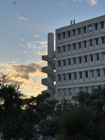 A modern building with a spiral staircase against a sunset sky. Surrounding greenery adds a natural touch to the urban scene.の写真素材