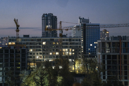 Construction site during twilight, featuring cranes and lit buildings, surrounded by a vibrant city skyline, emphasizing urban growth and architectural progressの写真素材