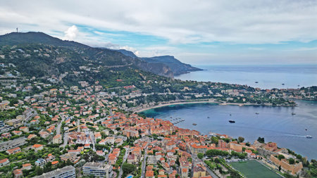 Scenic aerial perspective of a coastal town featuring terracotta roofs, green hills, and a tranquil bay, highlighting the blend of nature and urban lifeの写真素材