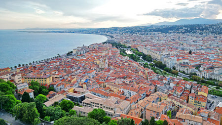 Aerial perspective of a coastal city featuring terracotta rooftops, green trees, and a tranquil waterfront, highlighting the blend of urban life and natureの写真素材